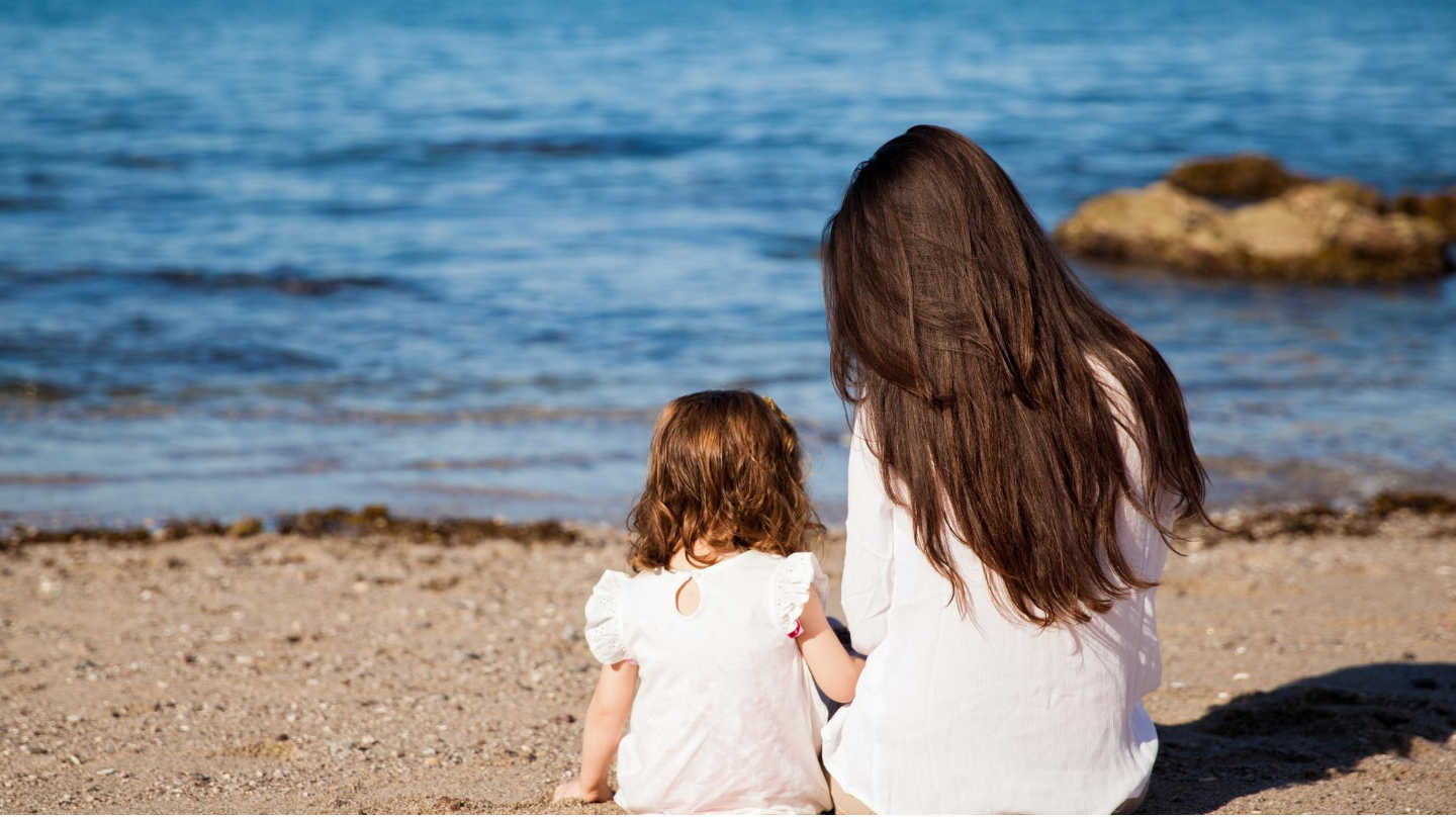 Une mère et sa fille vues de dos sur une plage face à la mer