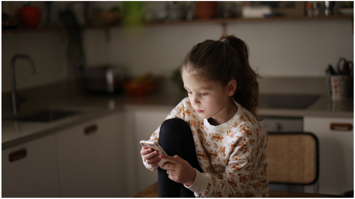Une jeune adolescente regarde son téléphone portable dans une cuisine.