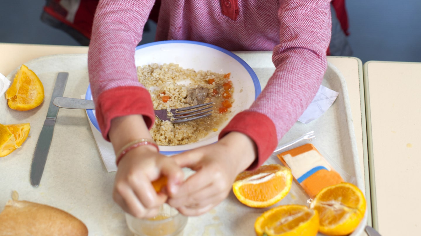 Des mains d'enfants au-dessus d'un plateau de cantine.