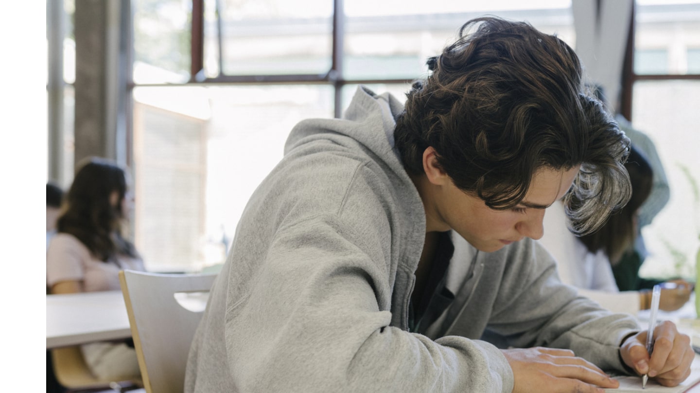 Un adolescent dans une salle de classe est penché en train d'écrire.