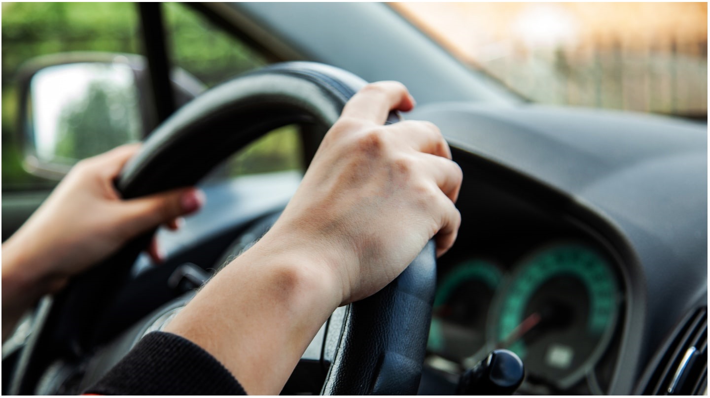 Deux mains posées sur le volant d'une voiture.