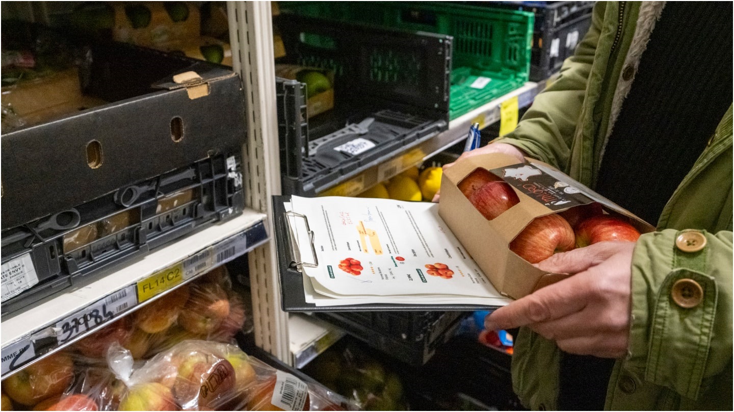 Un gros plan sur les mains d'un agent de la DGCCRF contrôlant l'origine de pommes dans un supermarché.