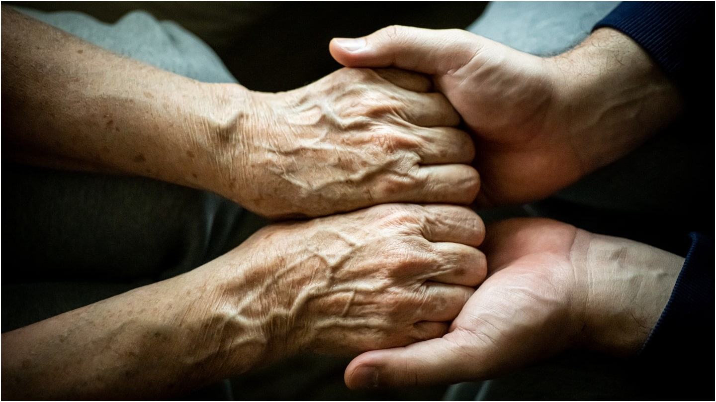 Une personne tenant les deux mains d'une personne plus âgée dans les siennes.