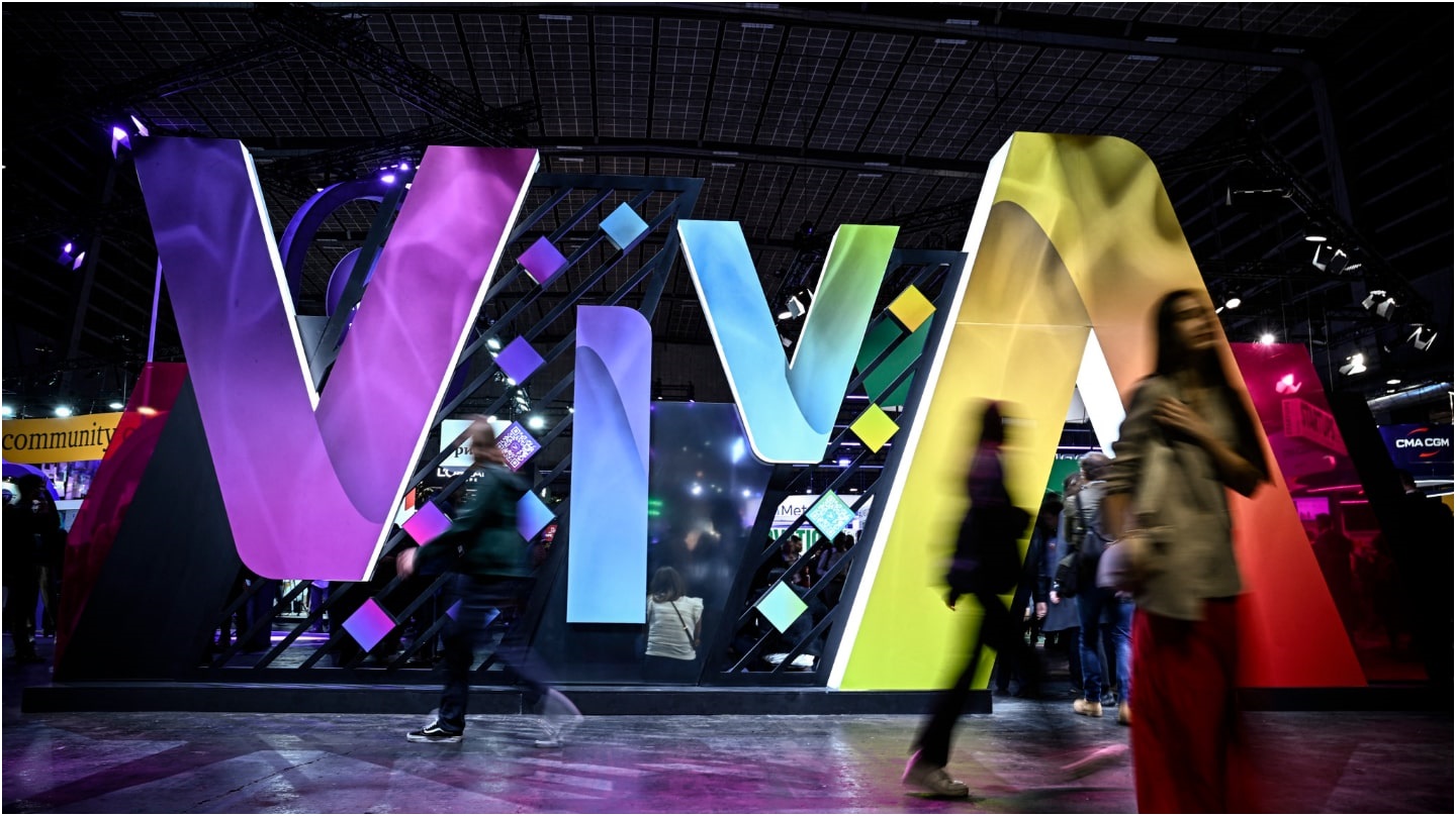 Des silhouettes floues passent devant des lettres géantes et colorées formant le mot « Viva ».