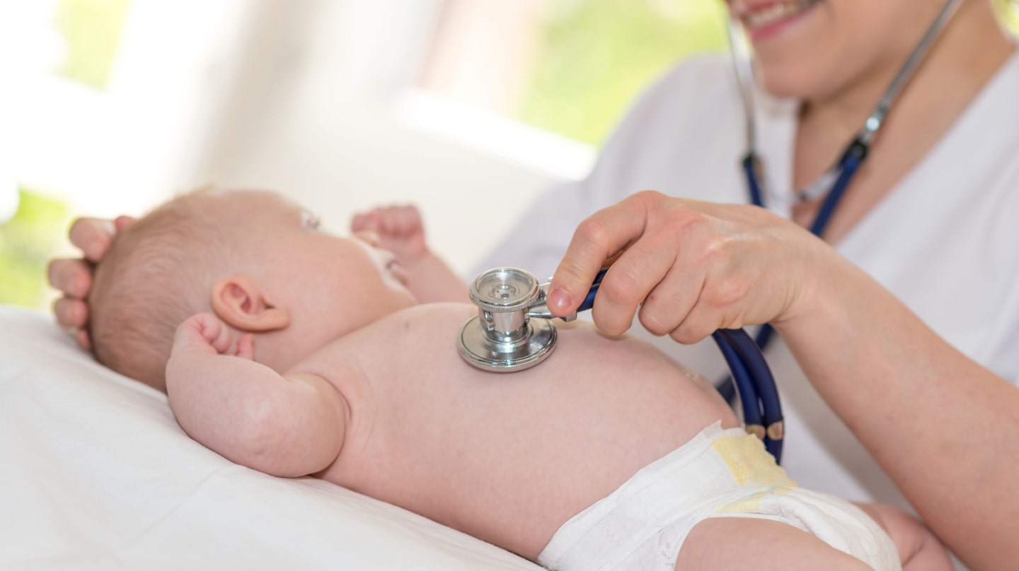 Un bébé en couche se fait examiner au stéthoscope par une femme en blouse blanche.