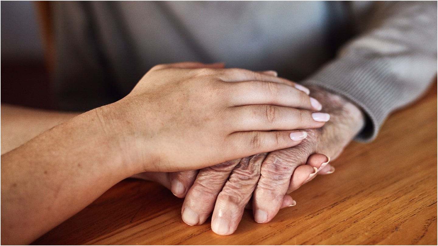 Des mains posées sur une table : une personne plus jeune réconforte une personne plus âgée.