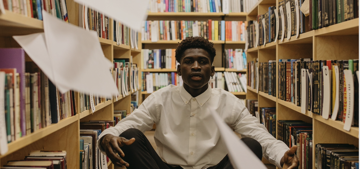 Un jeune homme est assis dans une bibliothèque.